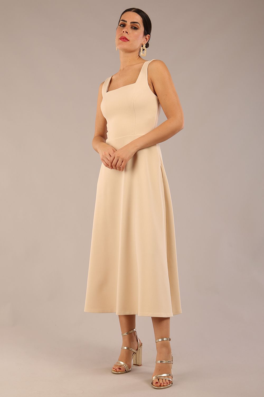 brunette model wearing a diva catwalk Tamsin Square Neckline Swing Dress sleeveless style with a midaxi  length and side pockets in Sandshell Beige colour front (Sandshell Beige)
