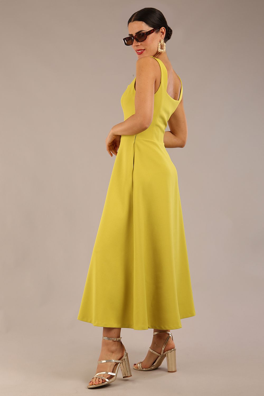 brunette model is wearing a diva catwalk Tamsin Square Neckline Swing Dress sleeveless style with a midaxi  length and side pockets in Citrus green colour front
