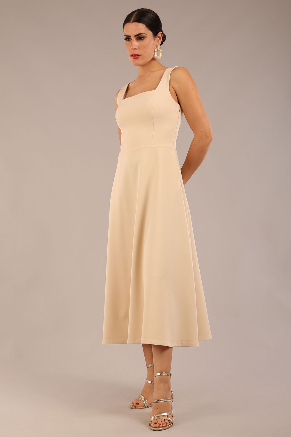 brunette model wearing a diva catwalk Tamsin Square Neckline Swing Dress sleeveless style with a midaxi  length and side pockets in Sandshell Beige colour front (Sandshell Beige)