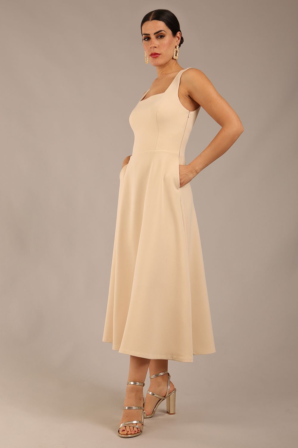 brunette model wearing a diva catwalk Tamsin Square Neckline Swing Dress sleeveless style with a midaxi  length and side pockets in Sandshell Beige colour front (Sandshell Beige)