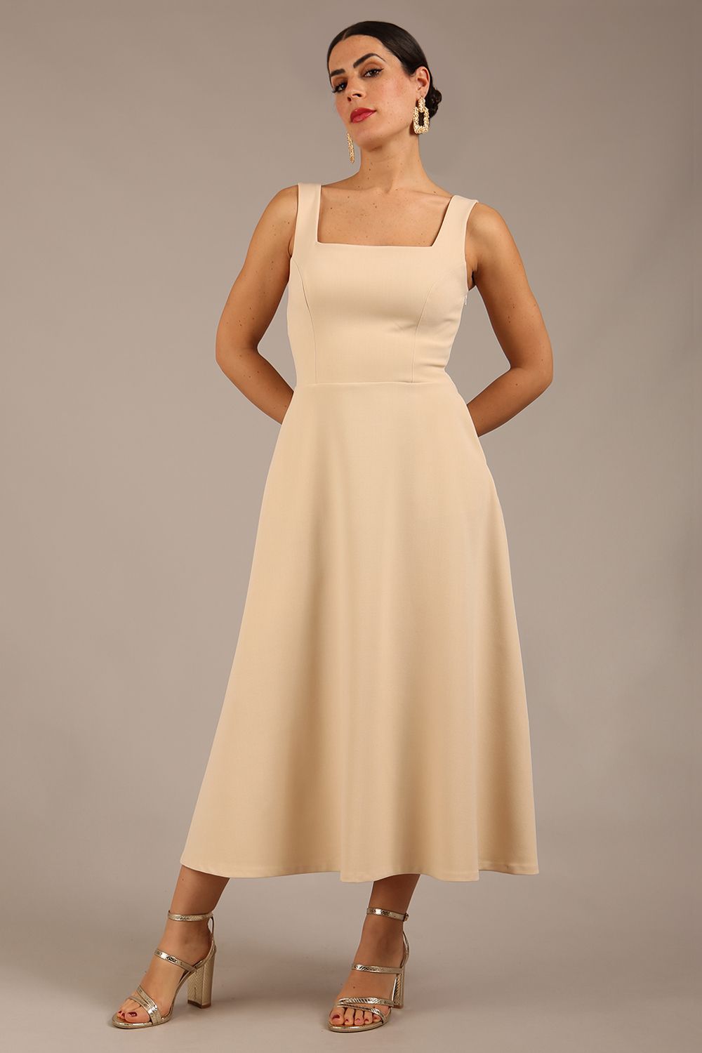 brunette model wearing a diva catwalk Tamsin Square Neckline Swing Dress sleeveless style with a midaxi  length and side pockets in Sandshell Beige colour front (Sandshell Beige)