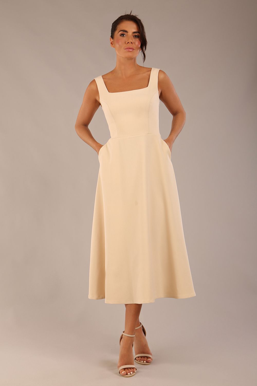 brunette model wearing a diva catwalk Tamsin Square Neckline Swing Dress sleeveless style with a midaxi  length and side pockets in Sandshell Beige colour front (Sandshell Beige)