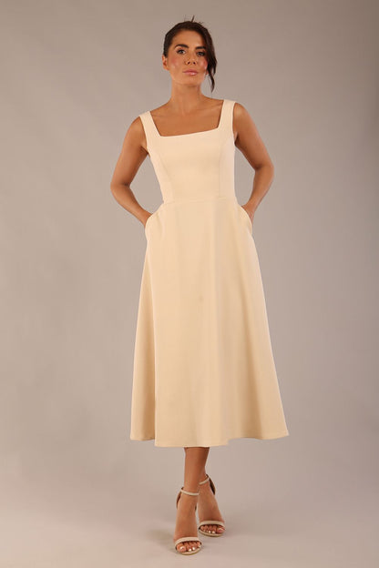brunette model wearing a diva catwalk Tamsin Square Neckline Swing Dress sleeveless style with a midaxi  length and side pockets in Sandshell Beige colour front (Sandshell Beige)