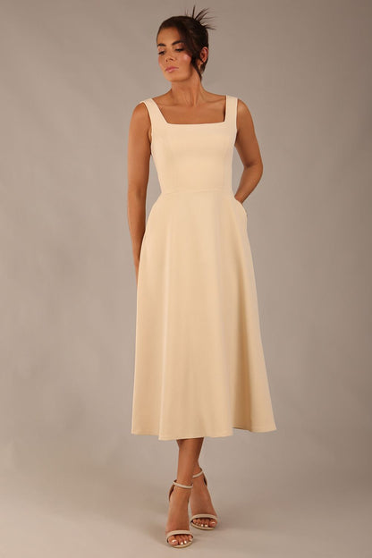 brunette model wearing a diva catwalk Tamsin Square Neckline Swing Dress sleeveless style with a midaxi  length and side pockets in Sandshell Beige colour front (Sandshell Beige)
