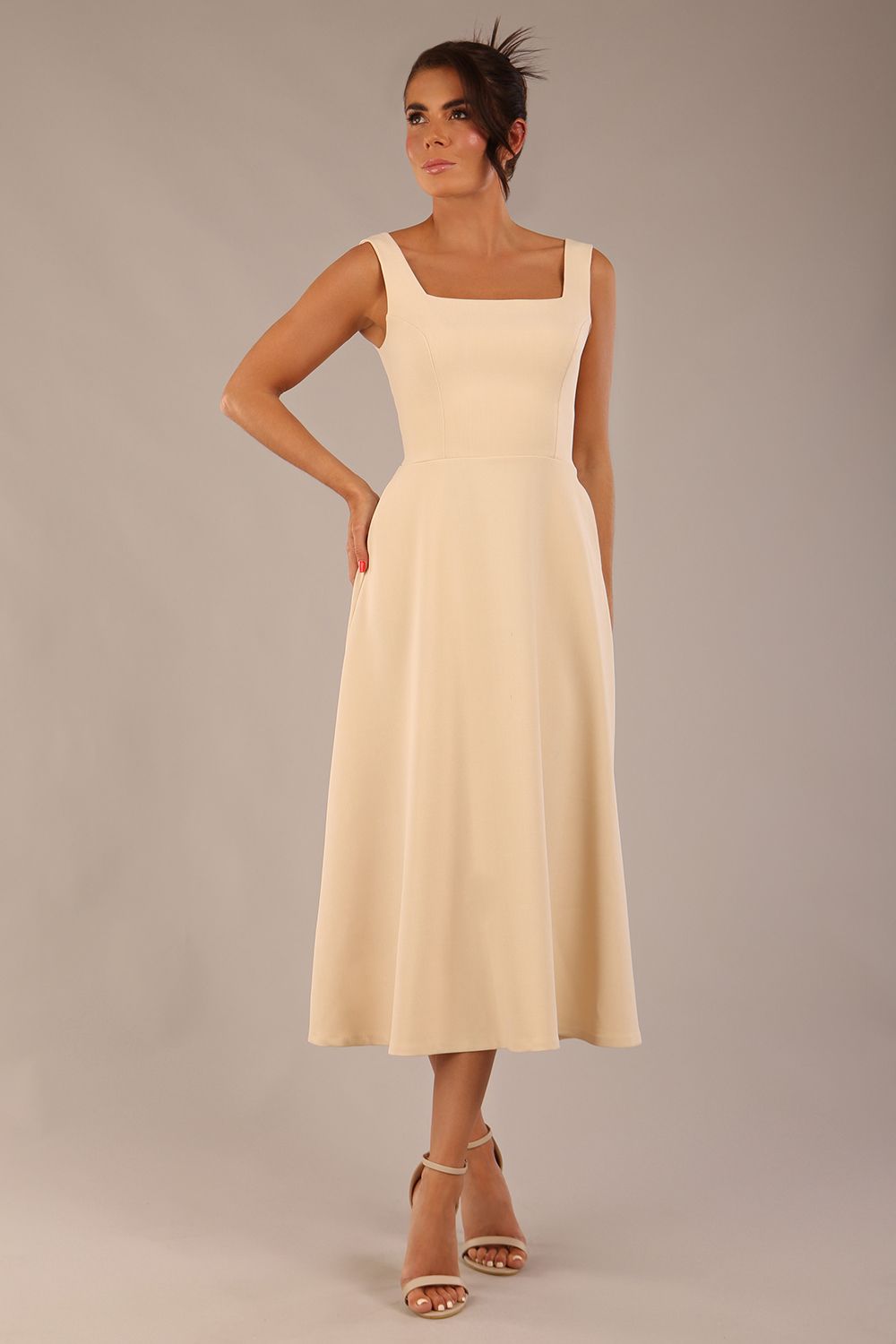 brunette model wearing a diva catwalk Tamsin Square Neckline Swing Dress sleeveless style with a midaxi  length and side pockets in Sandshell Beige colour front (Sandshell Beige)