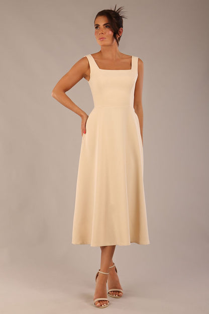 brunette model wearing a diva catwalk Tamsin Square Neckline Swing Dress sleeveless style with a midaxi  length and side pockets in Sandshell Beige colour front (Sandshell Beige)