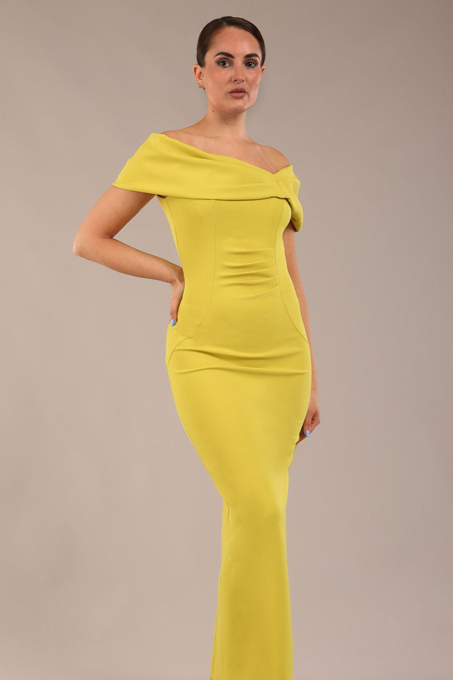 brunette model is wearing a diva catwalk Mariposa Longer Length Dress off the shoulder bardot neckline and midaxi length in citrus green colour front image