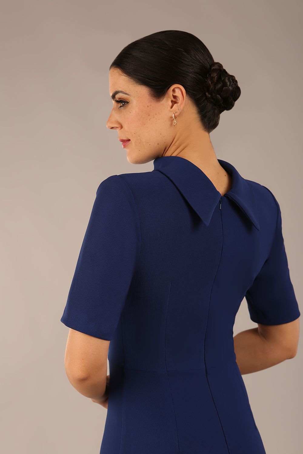 brunette model is wearing a diva catwalk Highmoor Short Sleeved Pencil Dress high neckline and shoulders pad in navy blue colour back image close up
