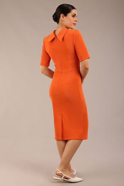 brunette model is wearing a diva catwalk Highmoor Short Sleeved Pencil Dress high neckline and shoulders pad in amber orange colour back image