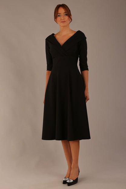 brunette model is wearing a diva catwalk Fabienne sleeved A-line Dress with pockets v neckline knee length wide waistband fold over v neckline in black colour front image (Black)