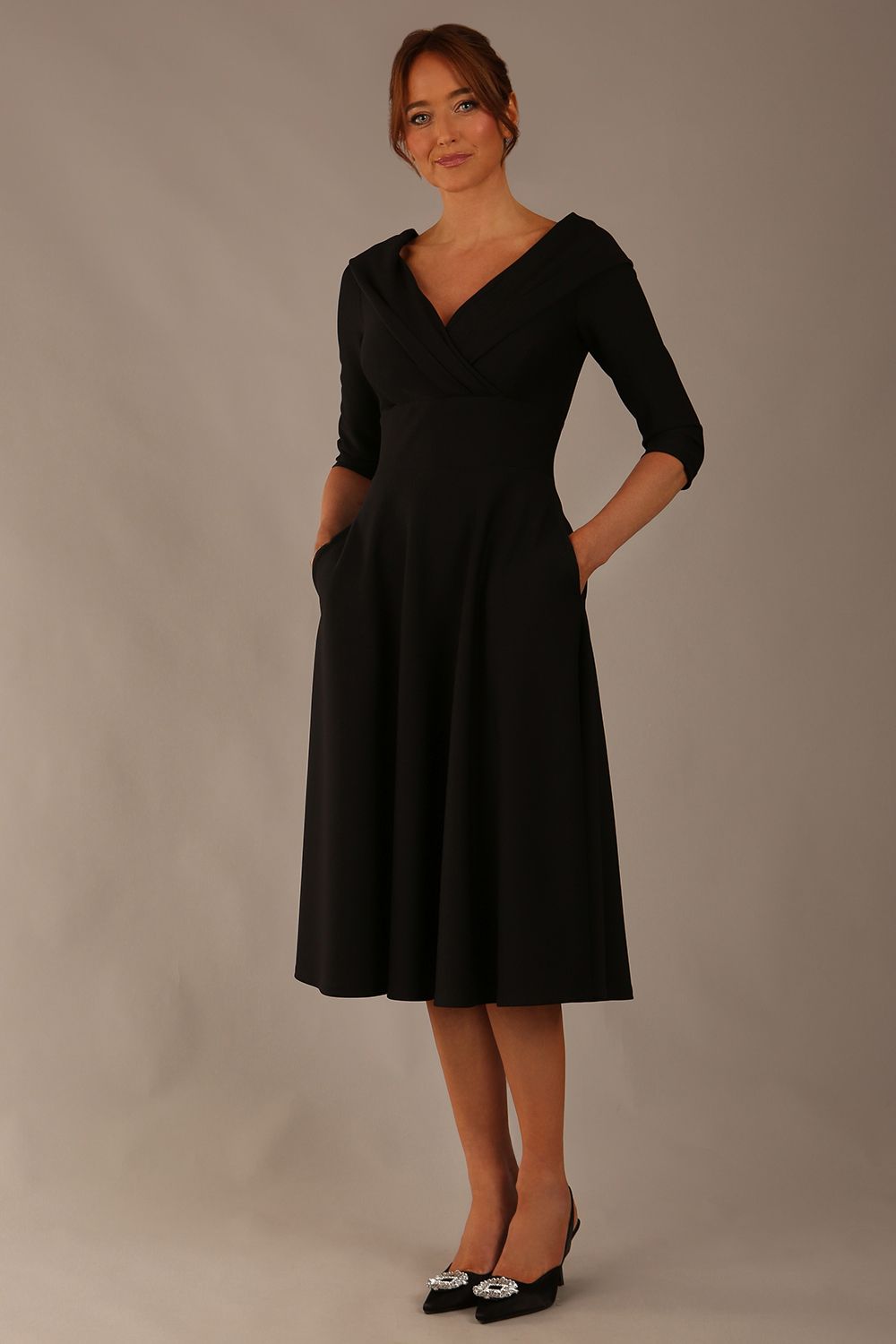 brunette model is wearing a diva catwalk Fabienne sleeved A-line Dress with pockets v neckline knee length wide waistband fold over v neckline in black colour front image (Black)