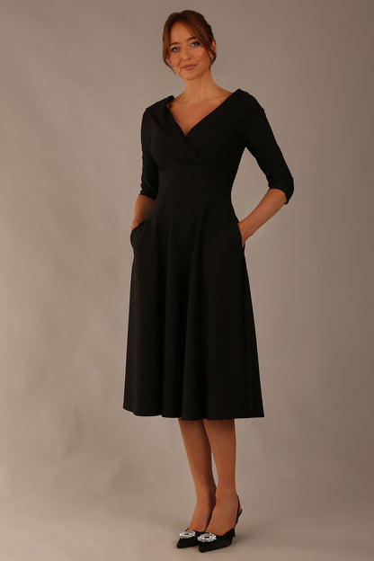 brunette model is wearing a diva catwalk Fabienne sleeved A-line Dress with pockets v neckline knee length wide waistband fold over v neckline in black colour front image (Black)