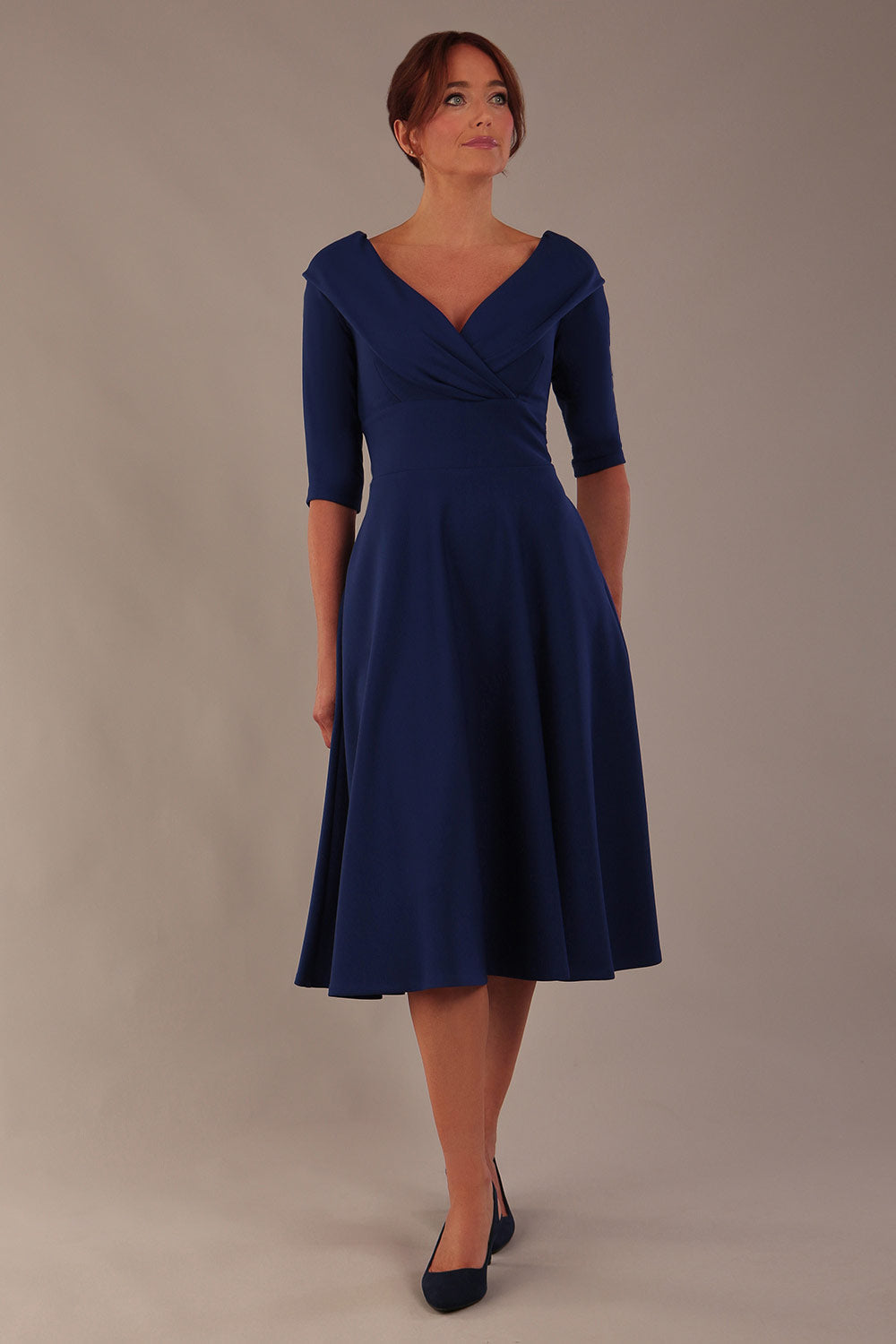 brunette model is wearing a diva catwalk Fabienne sleeved A-line Dress with pockets v neckline knee length wide waistband fold over v neckline in navy blue colour front image (Navy Blue)