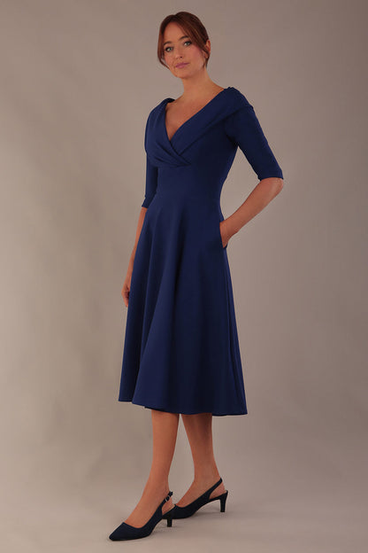 brunette model is wearing a diva catwalk Fabienne sleeved A-line Dress with pockets v neckline knee length wide waistband fold over v neckline in navy blue colour front image (Navy Blue)
