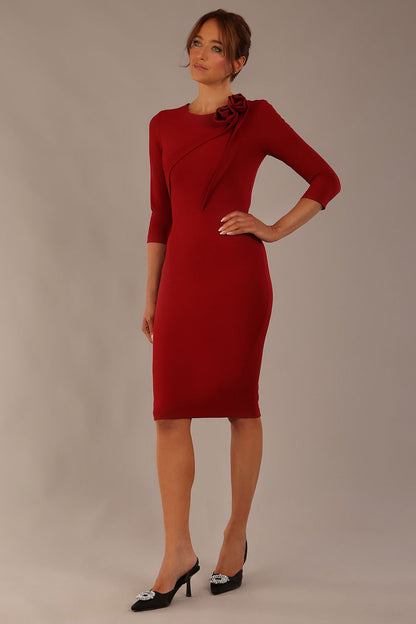 brunette model is wearing a diva catwalk Mirabelle ¾ Sleeves & Floral Shoulder Detail Pencil Dress with diagonal pleating across the front knee length in rosewood red colour front image