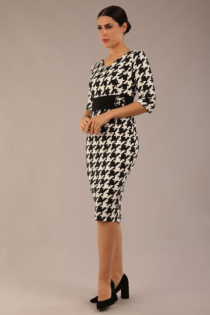 brunette model is wearing a diva catwalk OP-ART V-Neck Sleeved Monochrome Pencil Dress with black waistband and flower detail in a Super stretch dogtooth fabric black and white print front image