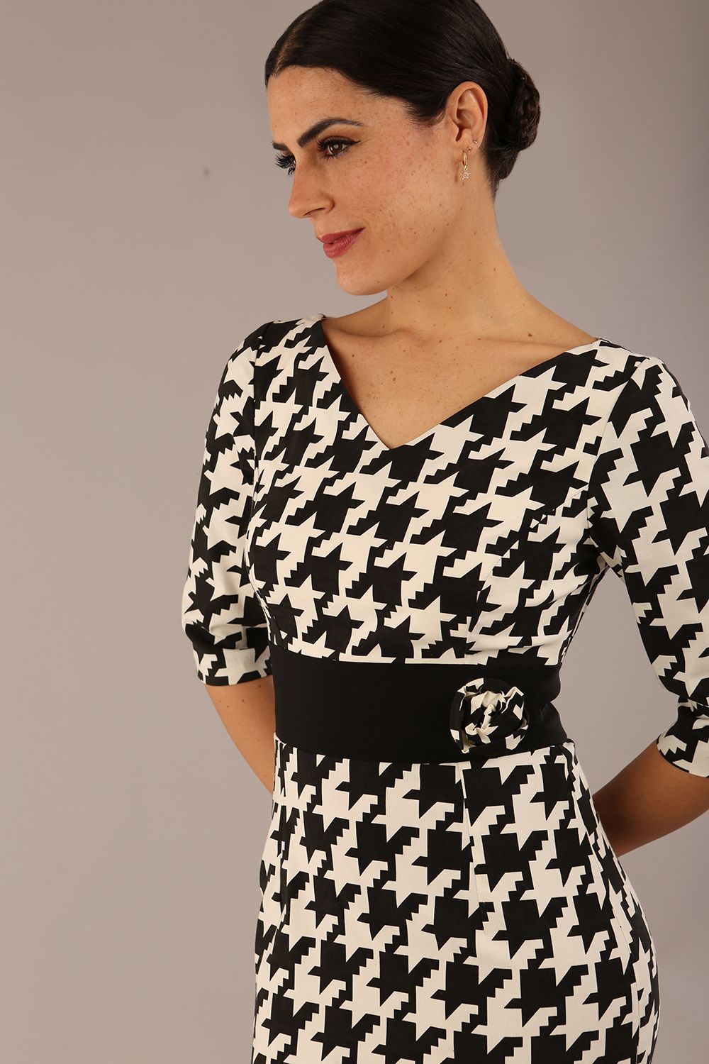 brunette model is wearing a diva catwalk OP-ART V-Neck Sleeved Monochrome Pencil Dress with black waistband and flower detail in a Super stretch dogtooth fabric black and white print front image