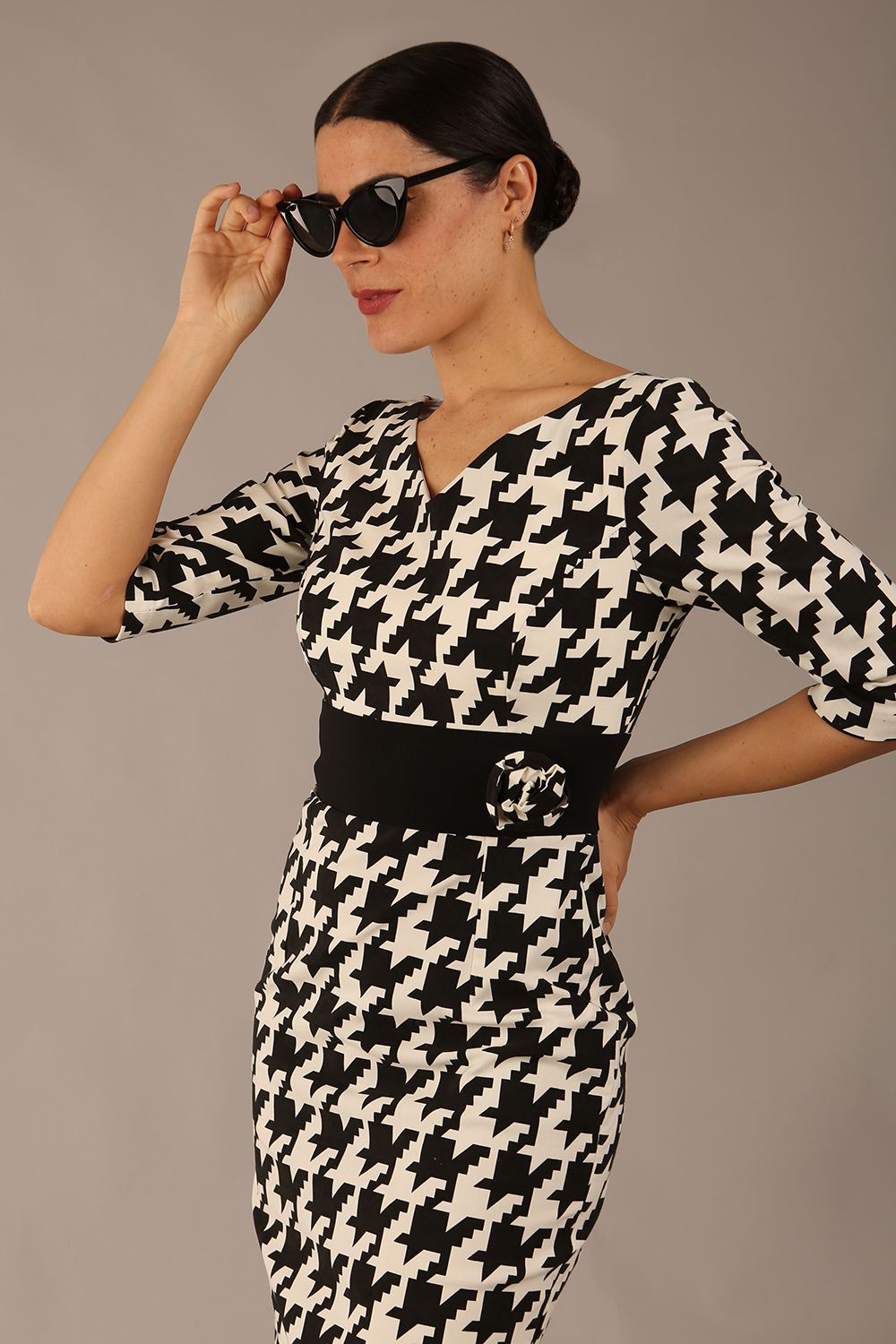 brunette model is wearing a diva catwalk OP-ART V-Neck Sleeved Monochrome Pencil Dress with black waistband and flower detail in a Super stretch dogtooth fabric black and white print front image
