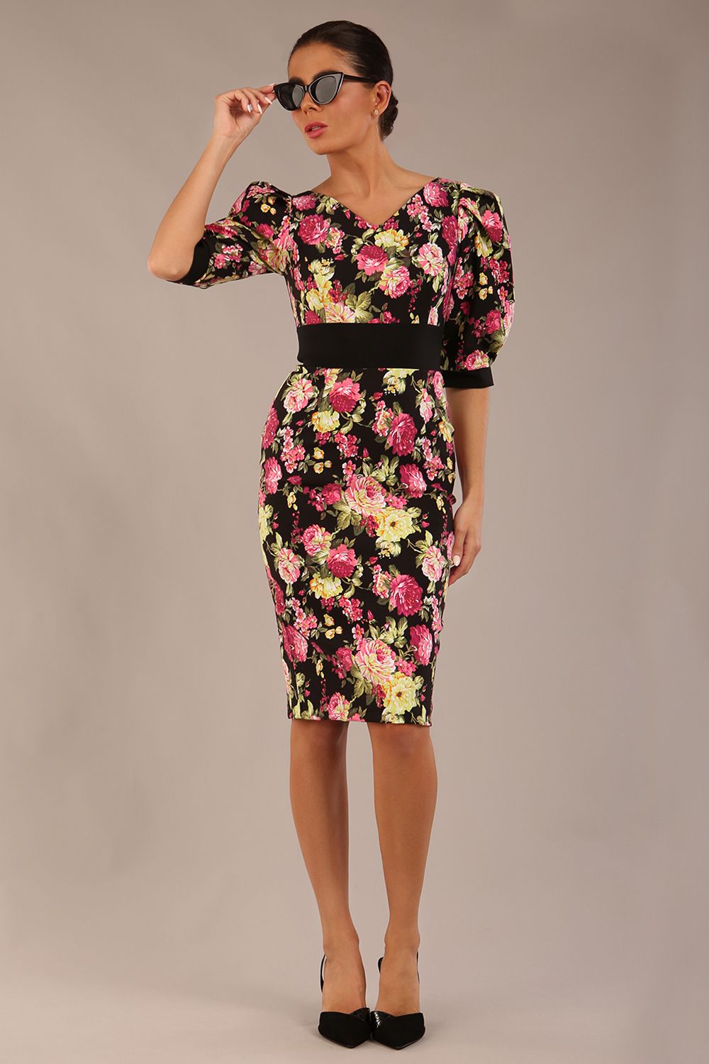 The brunette model is wearing a 7004 diva catwalk  Somerset Floral with Puff Sleeves & Black Waistband v neckline and knee length Pencil Dress in Black Spring Flower print front image