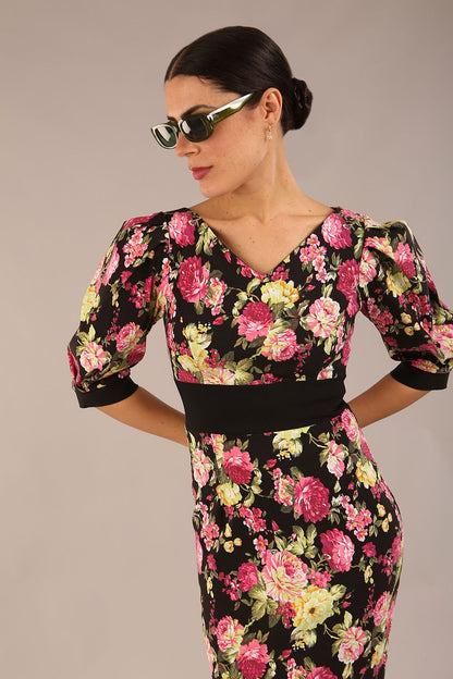 The brunette model is wearing a 7004 diva catwalk  Somerset Floral with Puff Sleeves & Black Waistband v neckline and knee length Pencil Dress in Black Spring Flower print front image