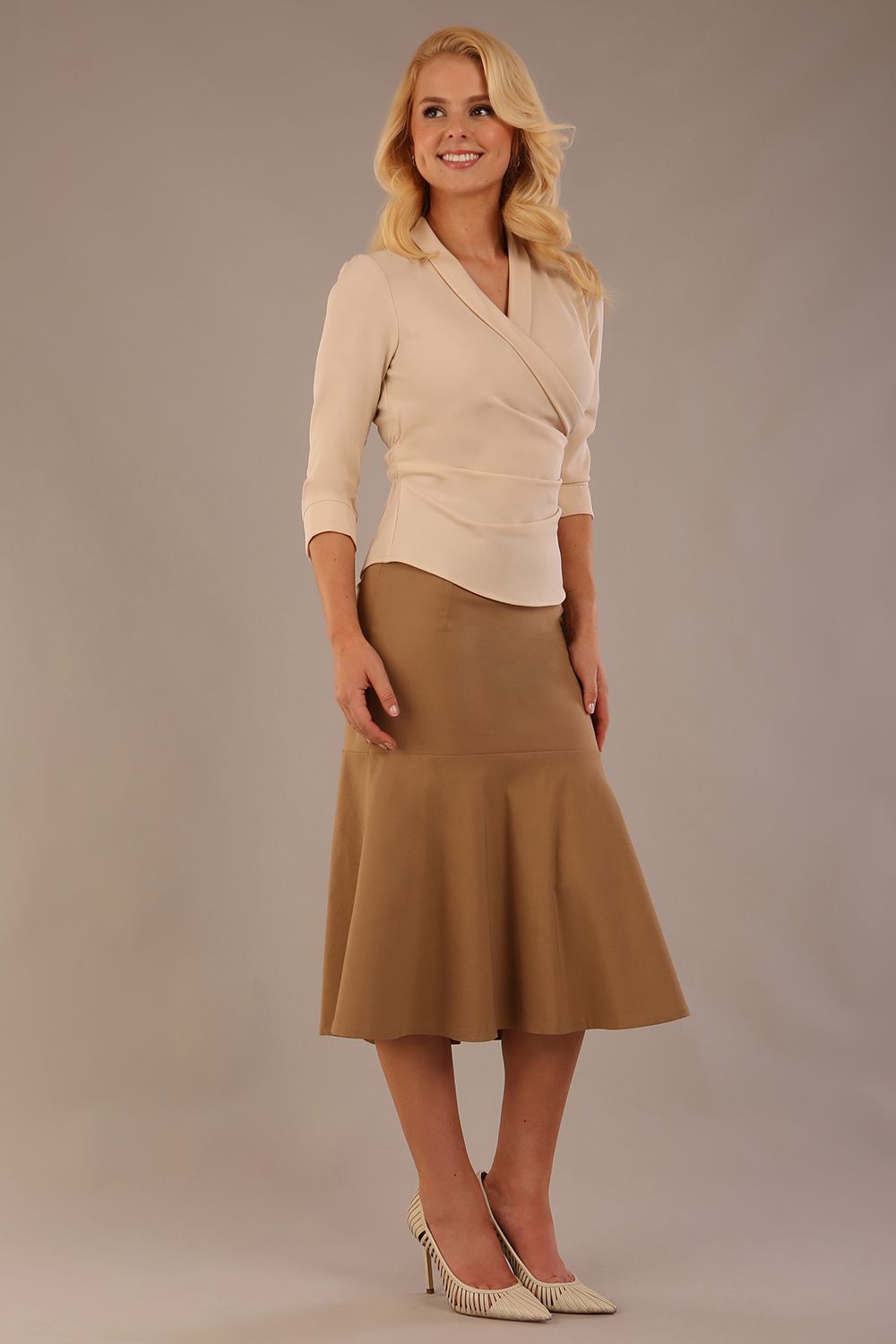 Model wearing a Trina wrap top in almond cream, with a wide V-neck and 3/4 sleeves, styled with a camel fishtail skirt (Almond Cream)