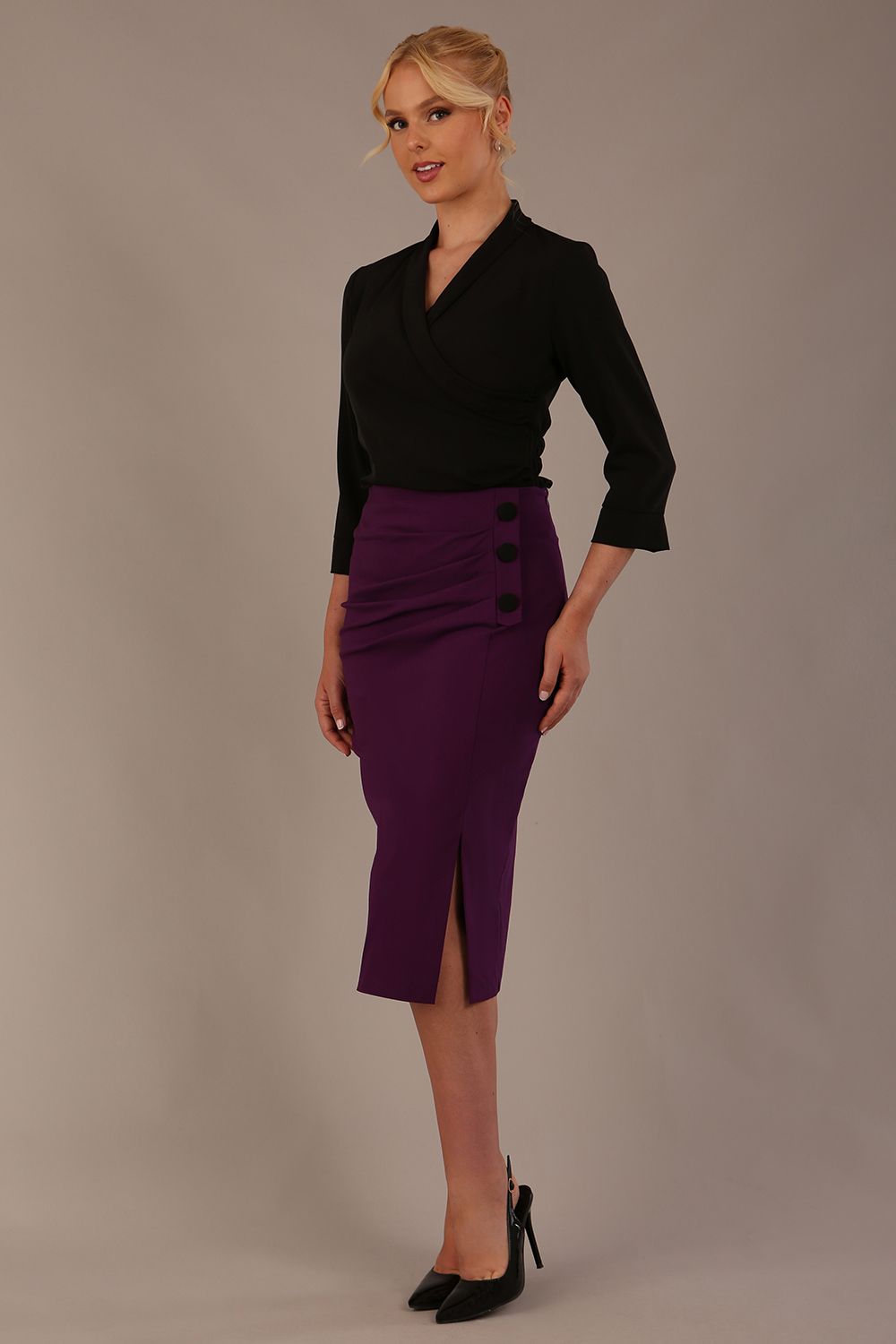 Model wearing a Trina wrap top in black, with a wide V-neck and 3/4 sleeves, styled with a purple pencil skirt front view (Black)
