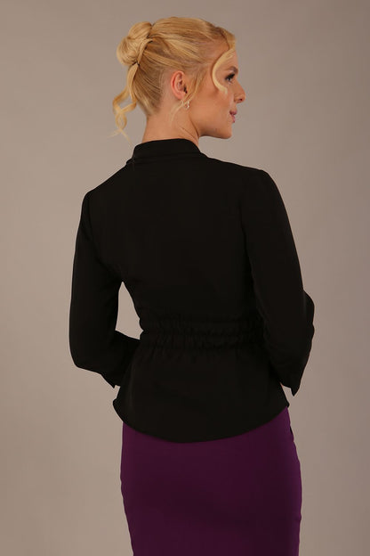 Model wearing a Trina wrap top in black, with a wide V-neck and 3/4 sleeves, styled with a purple pencil skirt front view (Black)