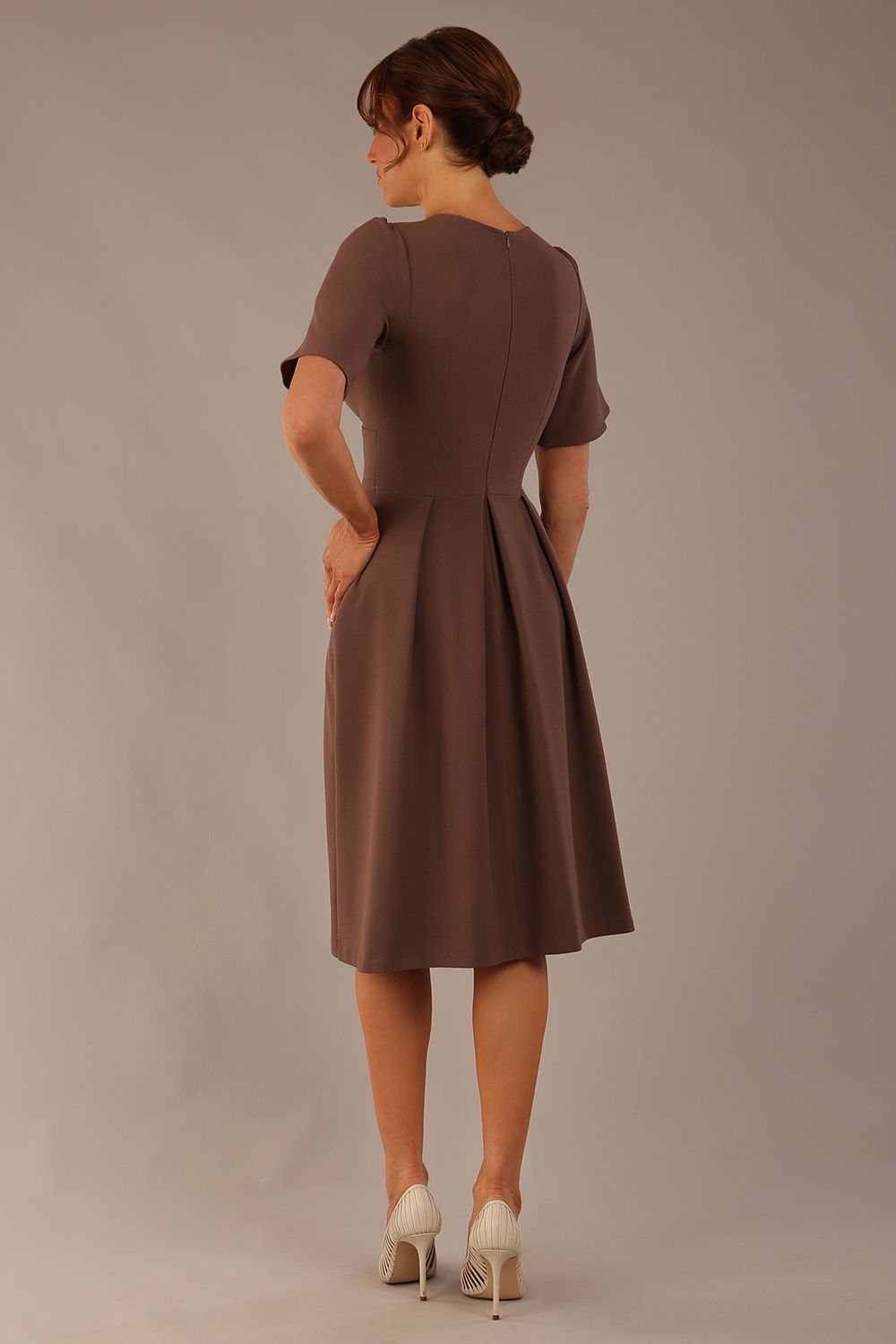 Woman wearing a brown dress against a plain background Close-up of the pleated bust detail and flared sleeves on the Dale dress in (Peppercorn Brown)