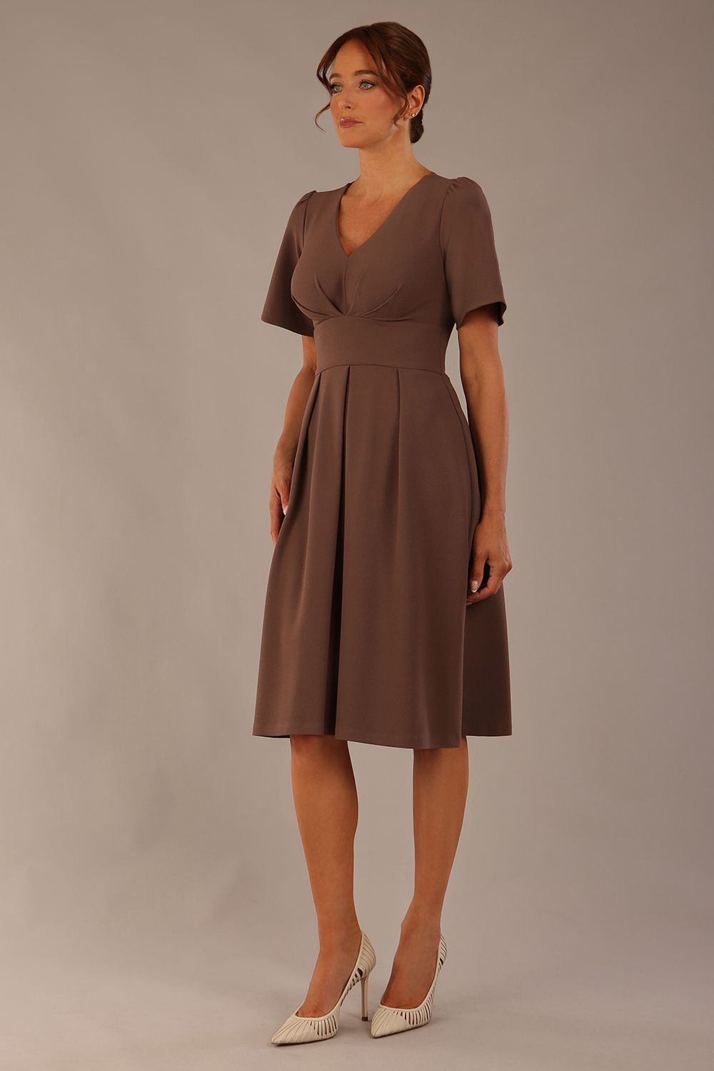 Woman wearing a brown dress against a plain background Close-up of the pleated bust detail and flared sleeves on the Dale dress in (Peppercorn Brown)