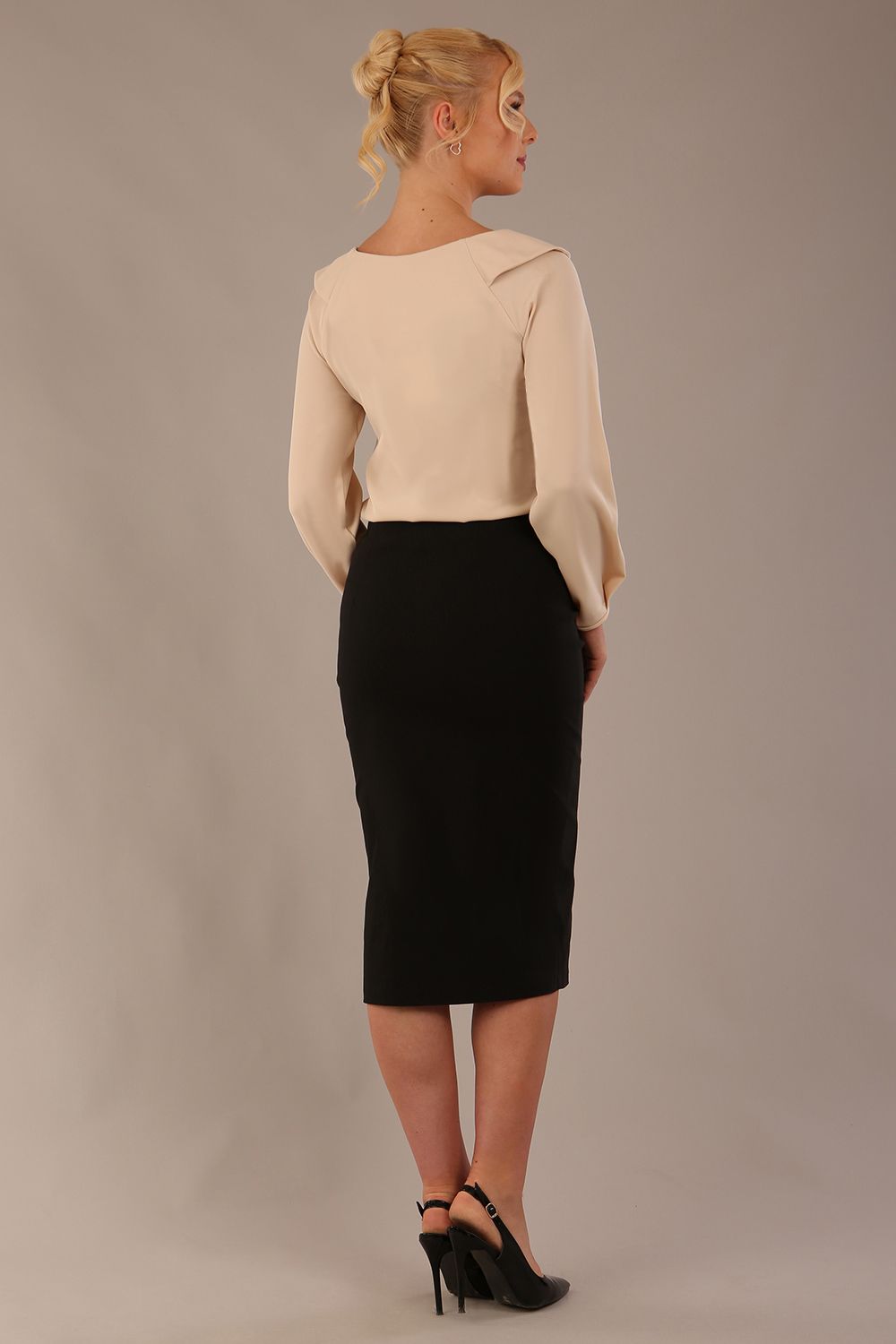 sitting model wearing a Cressida long sleeve top in almond cream, with a boat neckline and asymmetric bow, styled with a black skirt close up (Almond Cream)