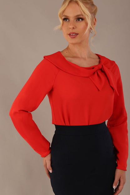model wearing a Cressida long sleeve top in poppy red, with a boat neckline and asymmetric bow, styled with a pencil skirt close up (Poppy Red)