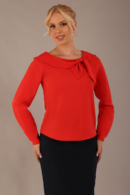 model wearing a Cressida long sleeve top in poppy red, with a boat neckline and asymmetric bow, styled with a pencil skirt close up (Poppy Red)