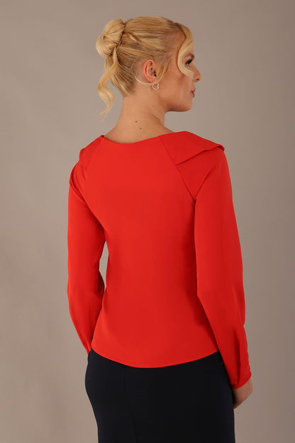 model wearing a Cressida long sleeve top in poppy red, with a boat neckline and asymmetric bow, styled with a pencil skirt close up (Poppy Red)