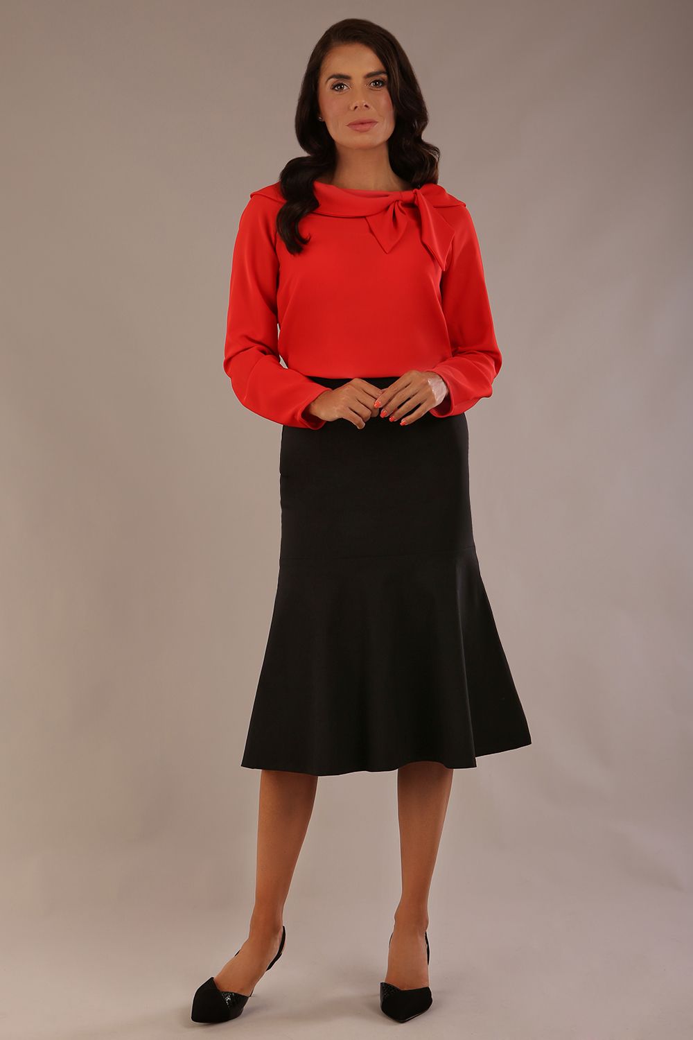 model wearing a Cressida long sleeve top in poppy red, with a boat neckline and asymmetric bow, styled with a pencil skirt close up (Poppy Red)