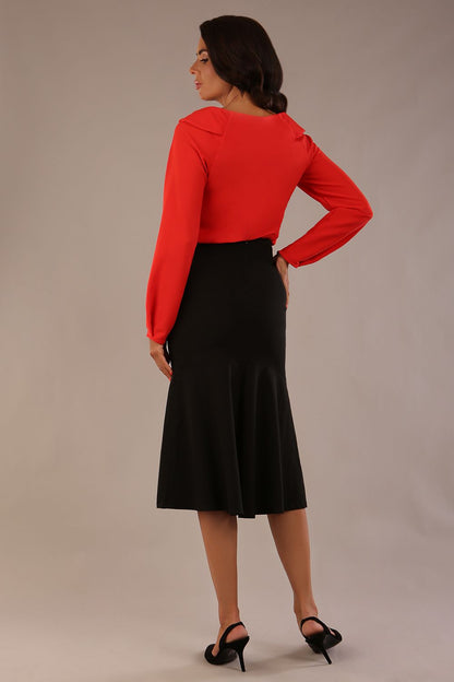 model wearing a Cressida long sleeve top in poppy red, with a boat neckline and asymmetric bow, styled with a pencil skirt close up (Poppy Red)