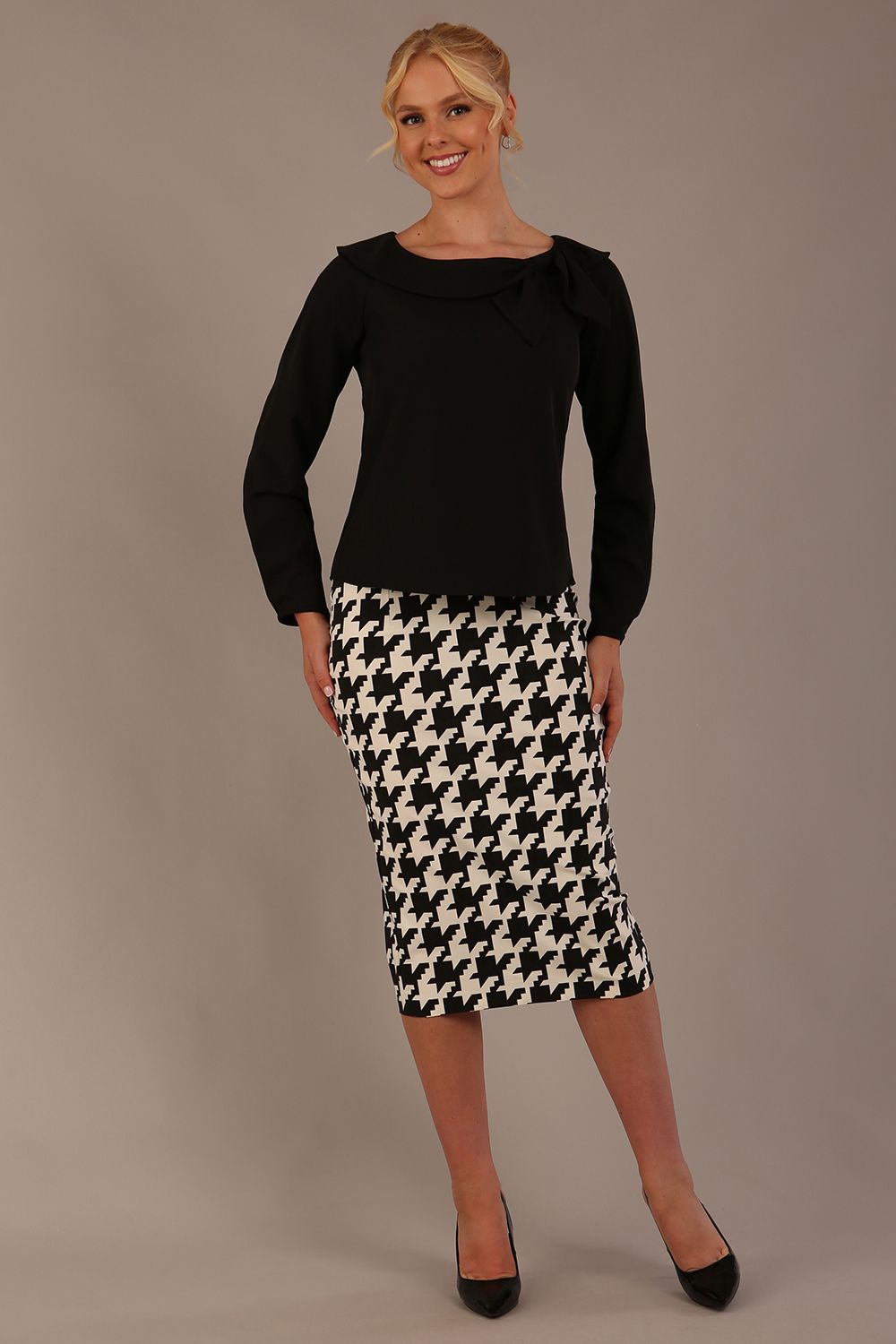 Woman wearing a diva catwalk cressida black top and houndstooth skirt against a neutral background (Black)