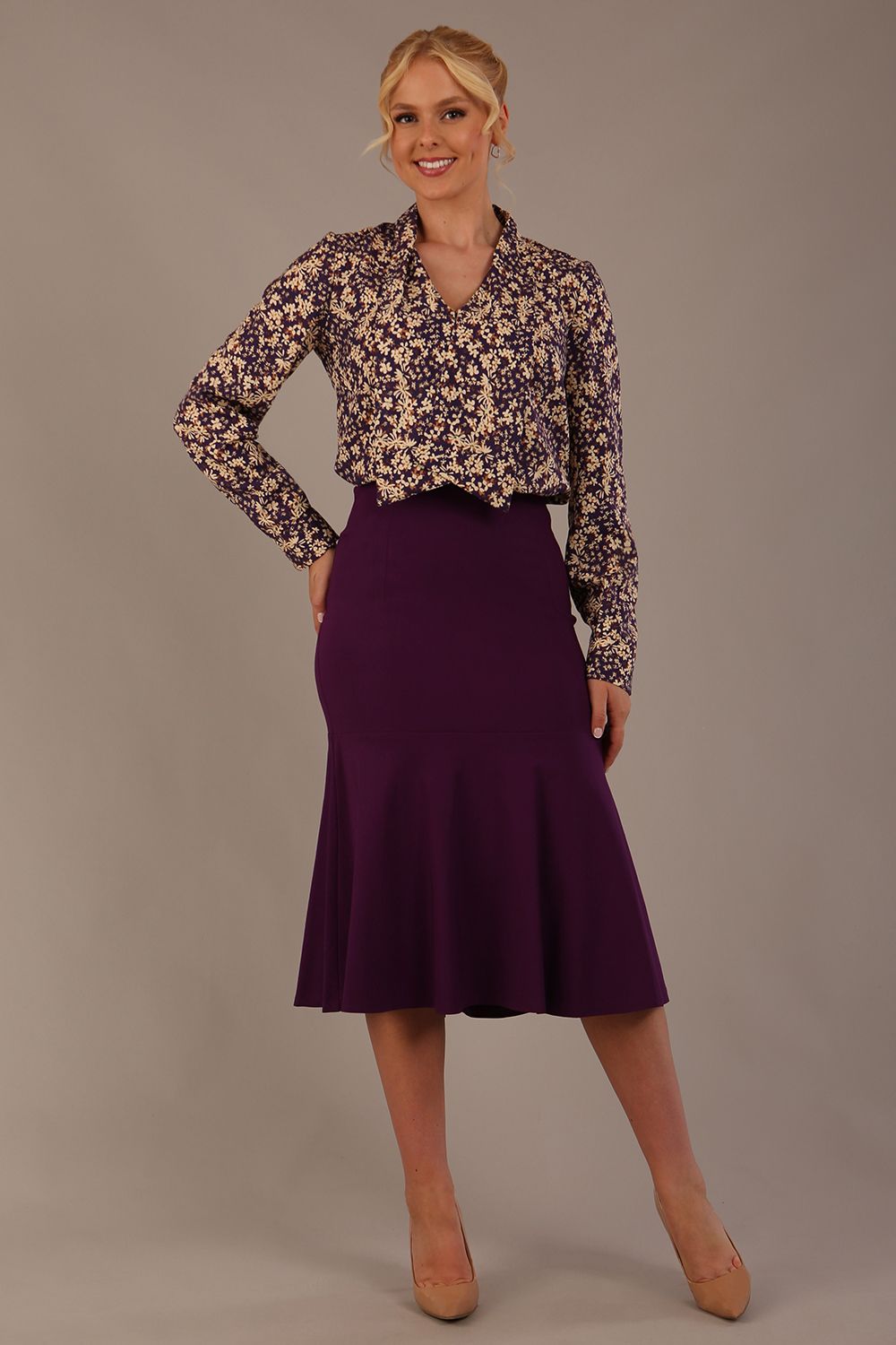 Model wearing the Truro floral top, showing the standard hip-length and draped V-neck and purple marlene skirt against a gray background (Purple)