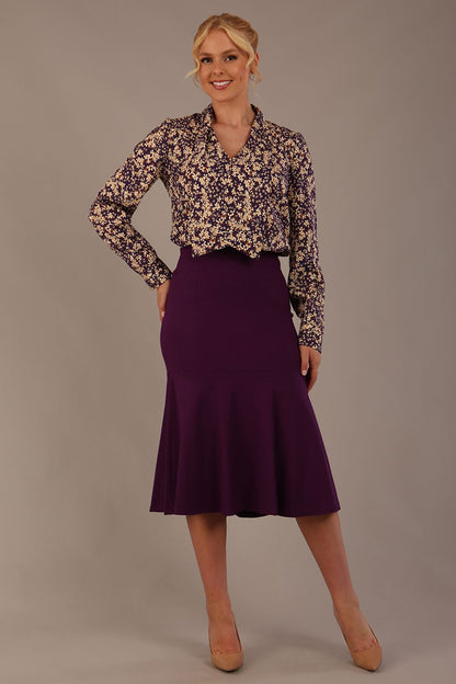 Model wearing the Truro floral top, showing the standard hip-length and draped V-neck and purple marlene skirt against a gray background (Purple)