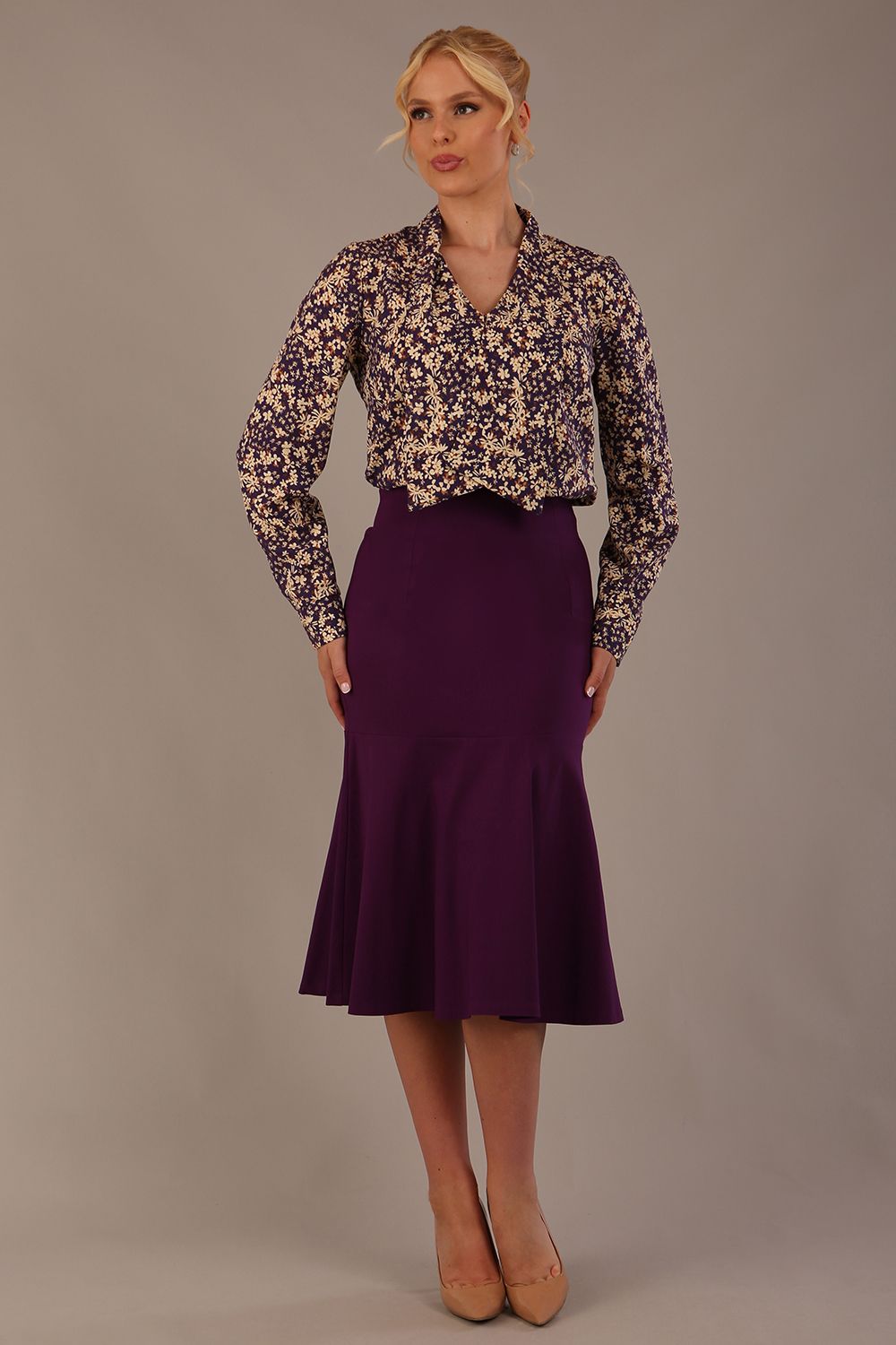 Model wearing the Truro floral top, showing the standard hip-length and draped V-neck and purple marlene skirt against a gray background (Purple)