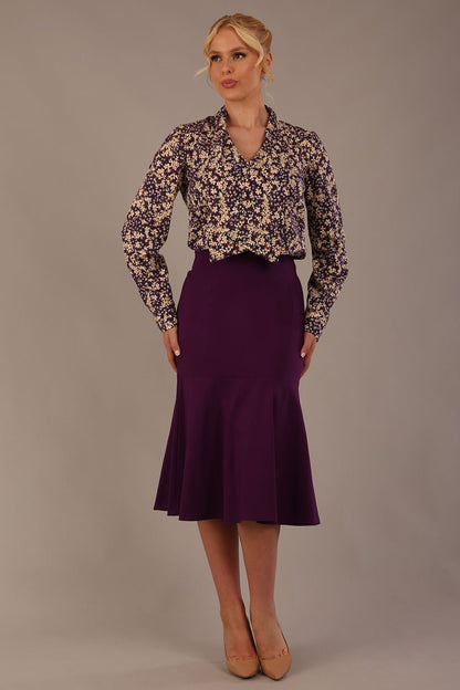 Model wearing the Truro floral top, showing the standard hip-length and draped V-neck and purple marlene skirt against a gray background (Purple)