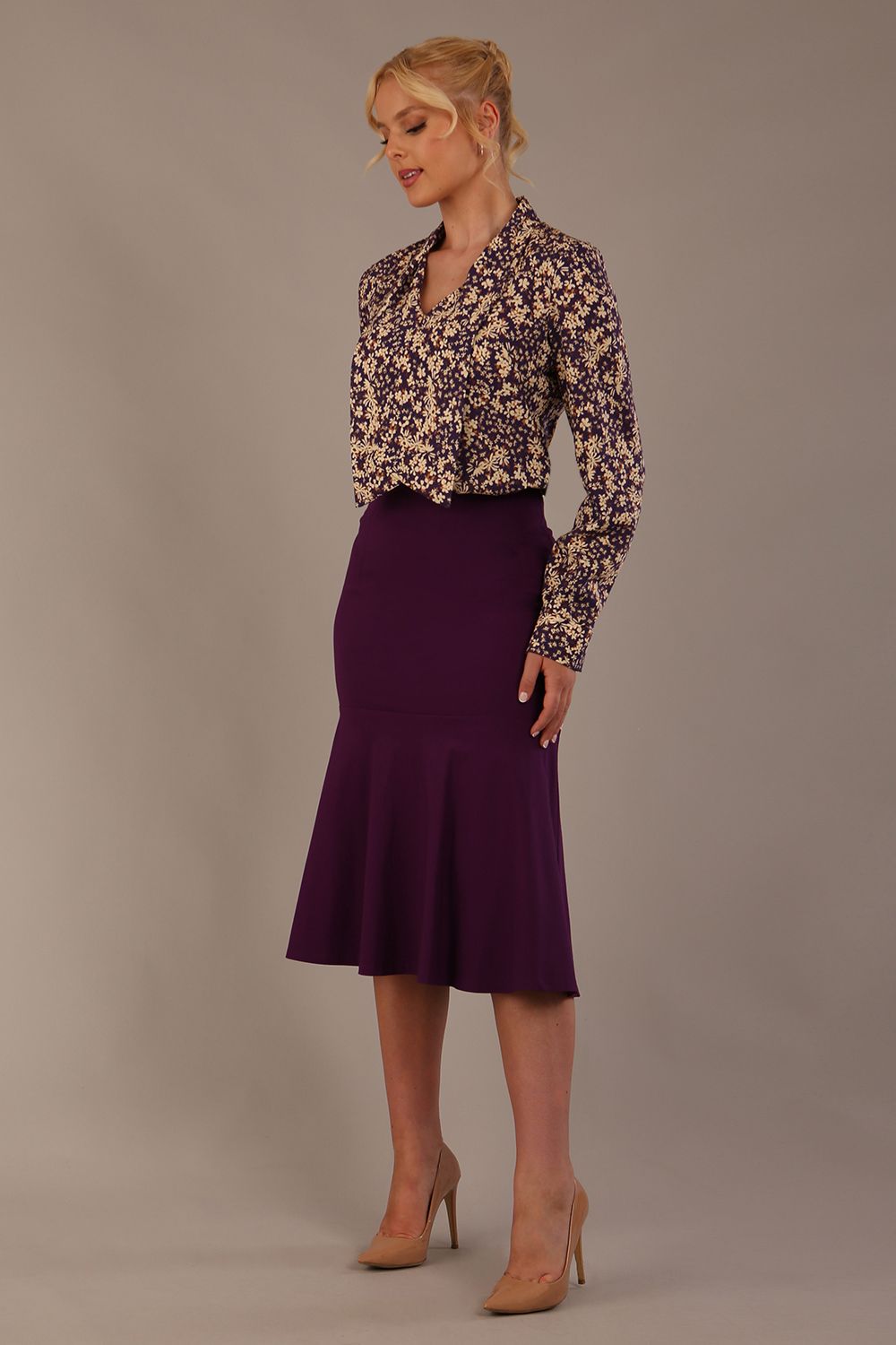 Woman wearing a floral blouse with a plain background: The Truro top's unique draped V-neck with its two elegant front ties. Close-up view (Meadow Mischief Print)