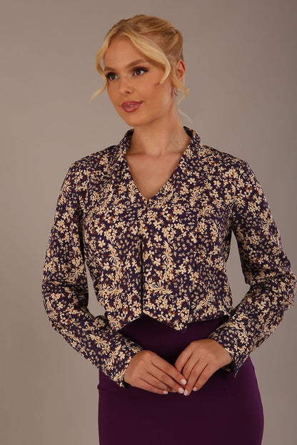 Woman wearing a floral blouse with a plain background: The Truro top's unique draped V-neck with its two elegant front ties. Close-up view (Meadow Mischief Print)