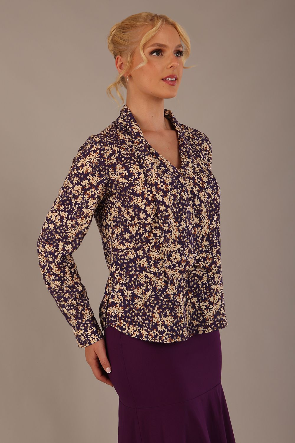 Woman wearing a floral blouse with a plain background: The Truro top's unique draped V-neck with its two elegant front ties. Close-up view (Meadow Mischief Print)