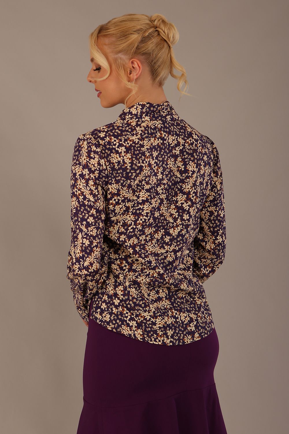 Woman wearing a floral blouse with a plain background: The Truro top's unique draped V-neck with its two elegant front ties. Close-up view (Meadow Mischief Print)