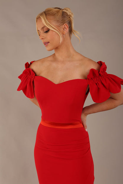 Woman wearing a red dress with ruffled sleeves in an elegant indoor setting. (Passion Red & Fire Orange Satin)