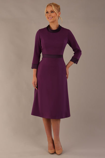Model wearing the Sybil A-line midi dress in imperial purple with a satin cowl neck and waistband. (Imperial Purple)