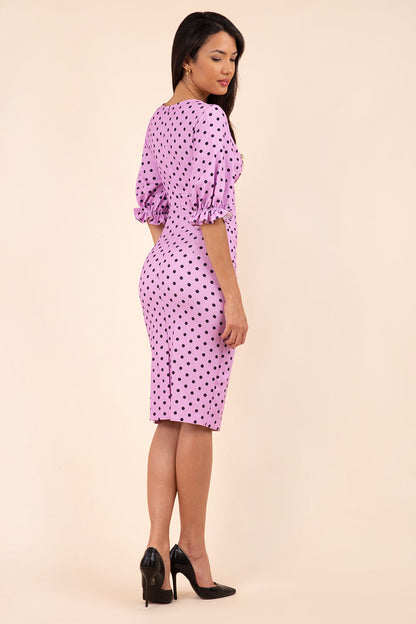 brunette model wearing diva catwalk palacio pencil fitted dress with three quarter puffed sleeve and pleating across the body with overlapping v-neckline in pink polka dot front