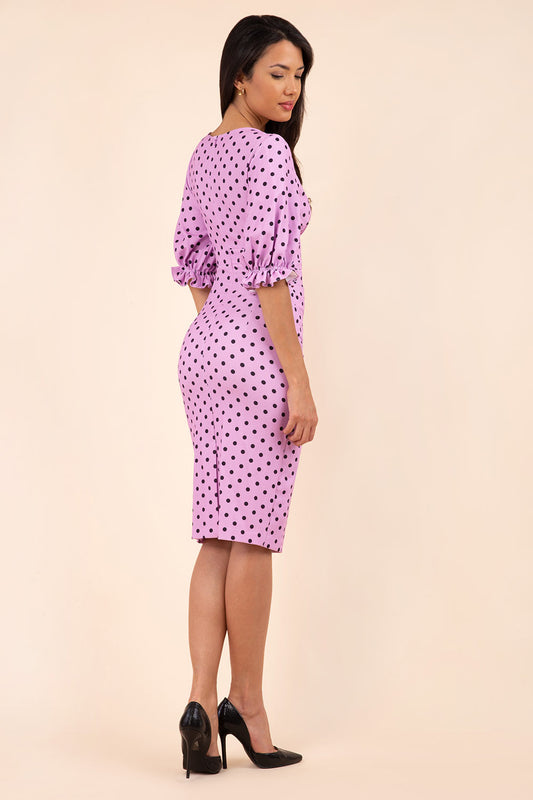 brunette model wearing diva catwalk palacio pencil fitted dress with three quarter puffed sleeve and pleating across the body with overlapping v-neckline in pink polka dot front