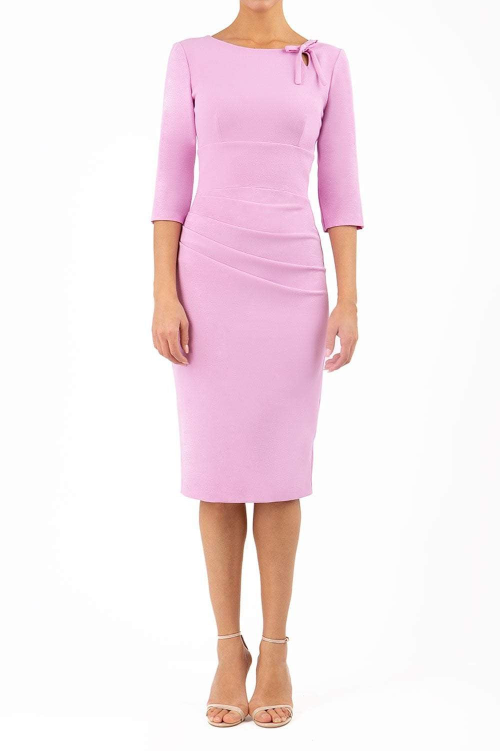 A model is wearing a three quarter sleeve pencil dress with a round neckline and bow detail at the front in pink