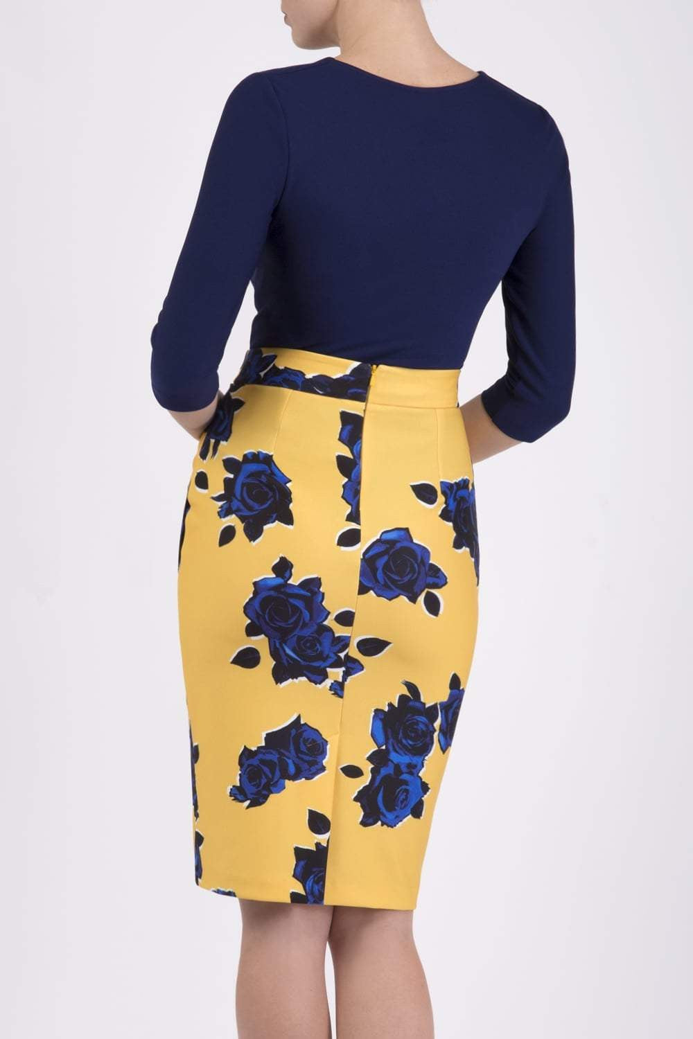 Woman wearing a navy top and yellow floral skirt on a city street.